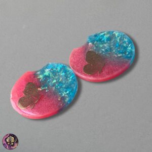 A pair of handmade butterfly glitter resin car coasters in pink and blue, displayed in a standard car cup holder
