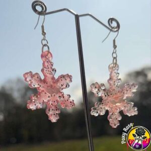 Close-up of pink glitter snowflake resin earrings on display card, festive and handmade for winter style.
