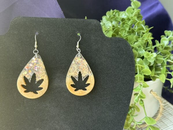 Handmade leaf-shaped resin earrings on a black display card, with visible chunky glitter and teardrop design.