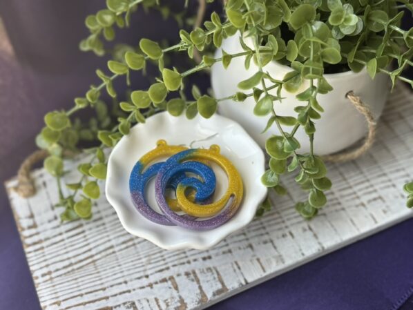 Colorful pinwheel earrings displayed in white dish, surrounded by faux greenery – glitter swirl resin dangles