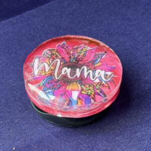 Close-up of handmade Mama phone grip featuring resin dome and multicolor glitter pattern
