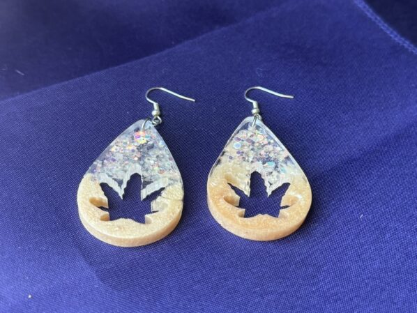 Glitter leaf teardrop resin earrings with gold and clear sparkle, shown flat against a deep blue background.