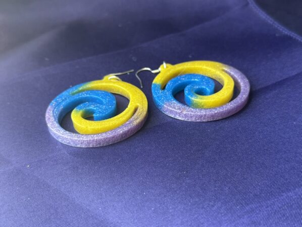 Colorful glitter swirl earrings viewed from side angle – handmade resin pinwheel earrings on purple fabric