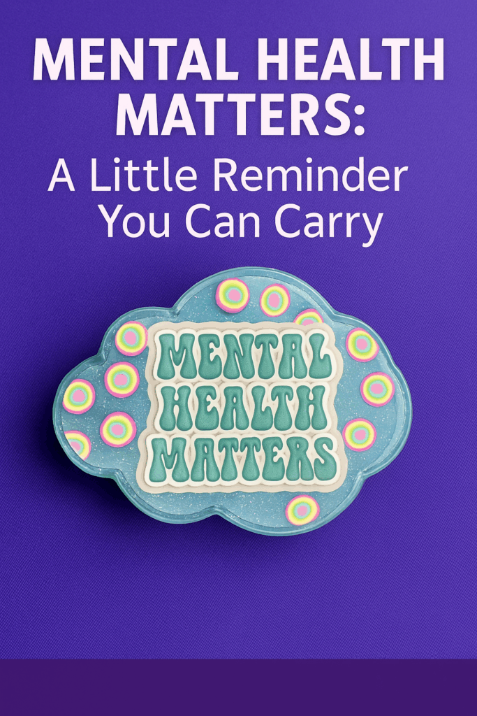 Cloud-shaped resin phone grip with “Mental Health Matters” quote, rainbow accents, and translucent blue finish displayed on an orange surface.