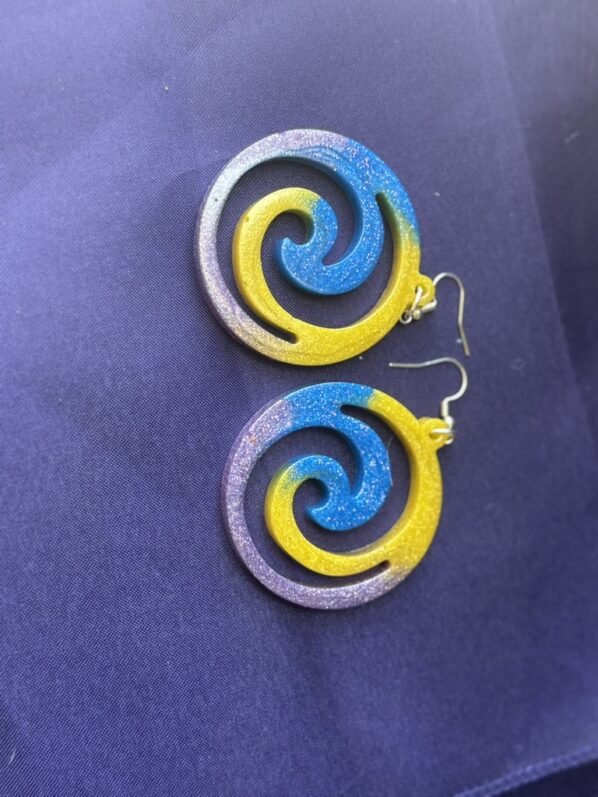 Swirl resin earrings in yellow, blue, and purple shown flat – vibrant glitter pinwheel design on purple background
