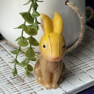 Yellow resin bunny placed on white wood surface with greenery, highlighting glossy finish and gem eyes